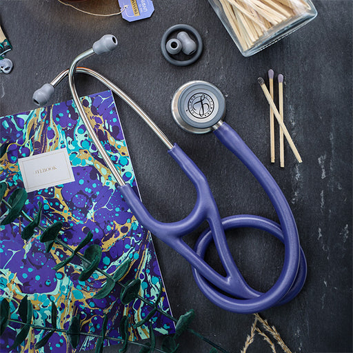 A blue 3M™ Littmann® Cardiology IV Diagnostic Stethoscope and a vibrant medical scrub top on a dark surface with earbuds and wooden sticks nearby.