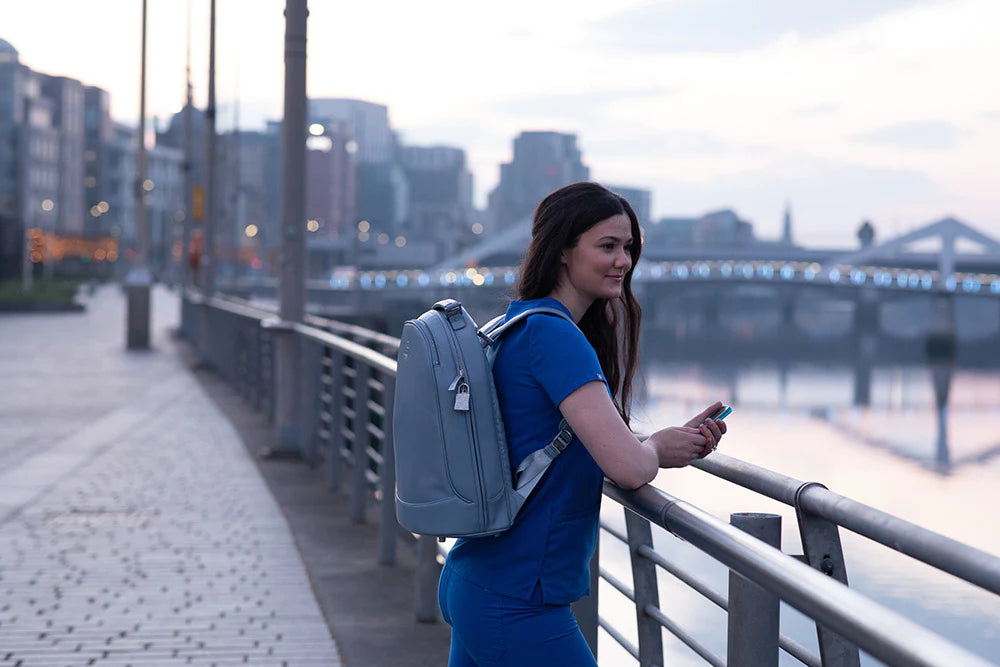 A professional woman with The Mae Medical Bag in Indigo by IYASU standing on a railing near a river.