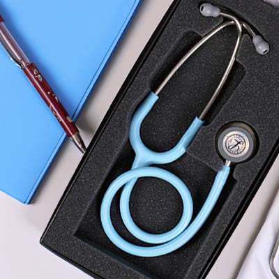 A 3M™ Littmann® Littmann Classic III Monitoring Stethoscope: Satin Marine Blue Tube 5912C, placed inside a black box, next to a blue folder and a red pen on a light blue surface.