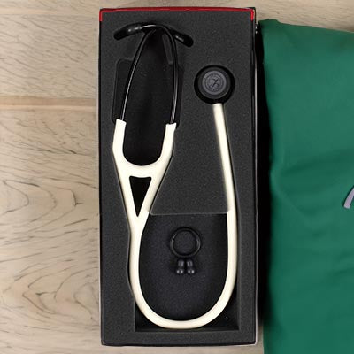 A white 3M™ Littmann® Cardiology IV Diagnostic Stethoscope: Satin Alabaster Tube 6186C and a reflex hammer inside a black and red storage box, placed on a wooden surface next to a green pillow.